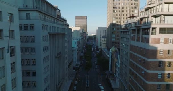 Grande rue en ville entourée de divers bâtiments à plusieurs étages. Structures hautes projetant l'ombre. Cape Town, Afrique du Sud — Video