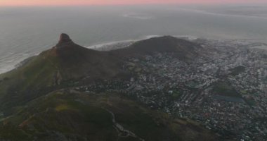 Okyanus kıyısındaki alacakaranlıktaki şehrin hava panoramik görüntüleri. Ufukta pembe bir gökyüzü var. Cape Town, Güney Afrika