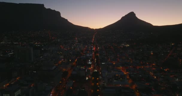 Imágenes panorámicas aéreas nocturnas del vecindario urbano. Silueta de picos de montaña contra el cielo crepuscular colorido. Ciudad del Cabo, Sudáfrica — Vídeo de stock