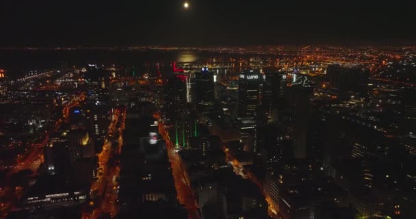 Лети над містом вночі. Колір освітлював вулиці і високі офісні будівлі в центрі міста. Морський порт у Табличній бухті на задньому плані. Кейптаун (ПАР) — стокове відео