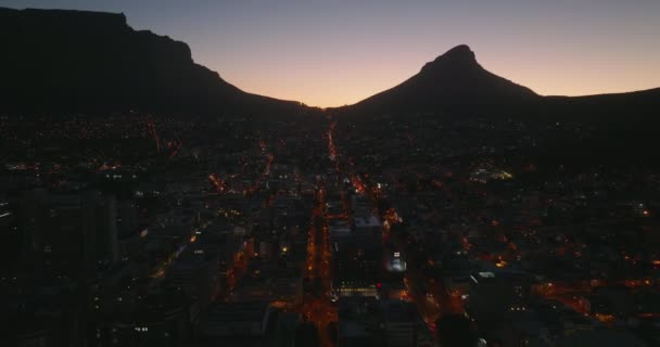 街路灯や山のシルエットのカラフルな夕暮れの空に照らされた長い直線通りと夜の街のロマンチックなショット。南アフリカ共和国ケープタウン — ストック動画