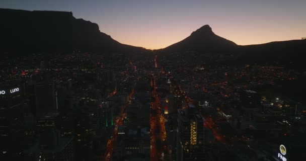 Voe acima da cidade noturna. Silhueta de montanhas contra céu crepúsculo pitoresco. Revelando para trás de edifícios de escritórios altos do centro da cidade. Cidade do Cabo, África do Sul — Vídeo de Stock