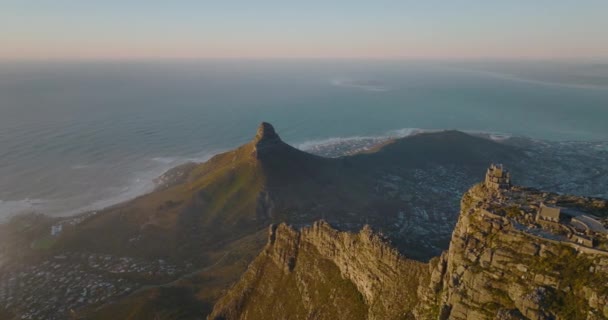 Слайд и панорамные кадры заостренной горы Львиная голова над морским побережьем. Летайте над Столовой горой и открывайте для себя дома в городском районе. Кейптаун, ЮАР — стоковое видео