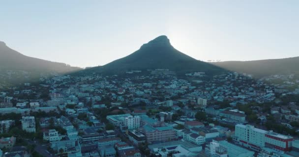 Vysoký špičatý vrchol vrhá stín na obytnou čtvrť ve městě. Vzdušné stoupající záběry odhalují jasné slunce za Lví hlavou. Kapské Město, Jihoafrická republika — Stock video