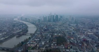 Sisli bir günde büyük şehrin hava panoramik görüntüleri. Şehrin içinden akan geniş bir nehir. Bir grup modern şehir merkezi gökdelenleri. Frankfurt am Main, Almanya