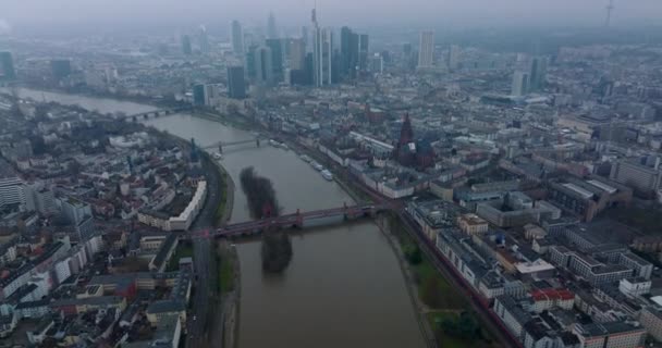 Vista ad alto angolo di costruzione nel quartiere urbano lungo il fiume. Inclinazione fino rivelare paesaggio urbano nebbioso con grattacieli del centro. Francoforte sul Meno, Germania — Video Stock