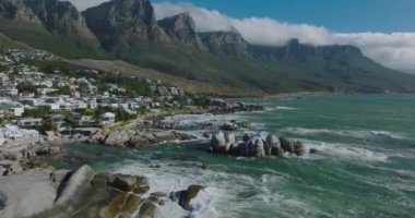 Sahilin üzerinden uç. Dalgaların kıyı kayalarına çarptığı dalgalı deniz. Yüksek dağ sırtının altındaki varoşlarda. Cape Town, Güney Afrika