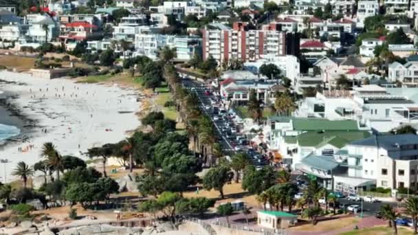 Sommarsemester destination. Byggnader i tropisk turistort och människor på sandstrand i Camps Bay. Vädret blåste på solig dag. Kapstaden, Sydafrika — Stockvideo