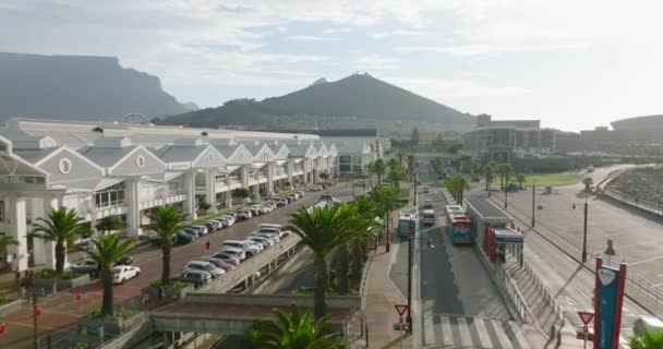 Zboară de-a lungul unui centru comercial mare pe Victoria și Alfred Waterfront. Trafic pe o stradă largă înconjurată de palmieri. Cape Town, Africa de Sud — Videoclip de stoc
