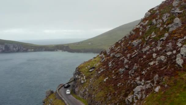 Voertuigen die elkaar passeren op een smalle weg die kronkelt langs een steile helling hoog boven de zeekust. Geweldige panoramische route rond Slea Head. Ierland — Stockvideo