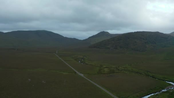 Rekaman panorama udara pemandangan dengan pegunungan di latar belakang. Arus berliku di sepanjang jalan lurus. Irlandia — Stok Video