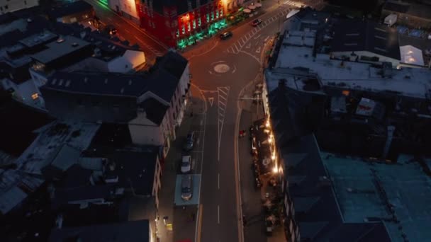 Vuela por encima de la calle iluminada de la ciudad. Coloridas fachadas de la casa a lo largo de la carretera en el centro de la ciudad por la noche. Killarney, Irlanda — Vídeos de Stock