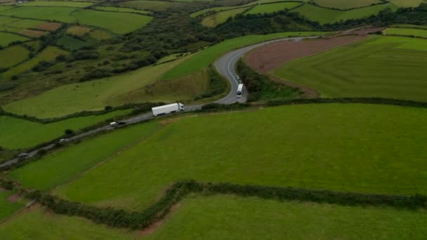 Wysoki kąt widzenia pojazdów jadących po drogach na wsi. Ciężarówka przejeżdżająca przed autobusem w krzywej. Zielone łąki i pastwiska. Irlandia — Wideo stockowe
