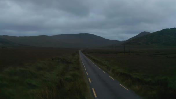 Schmale Straße mit gestrichelten Linien, die in der Abenddämmerung in der Landschaft Ränder markieren. Fliegen gegen Auto, das aus der Ferne kommt. Irland — Stockvideo