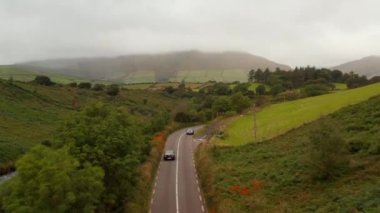 Kırsalda başka bir arabanın yanından geçen bir araba. Ağaçlar ve çalılarla çevrili dolambaçlı yolda takip aracı. İrlanda
