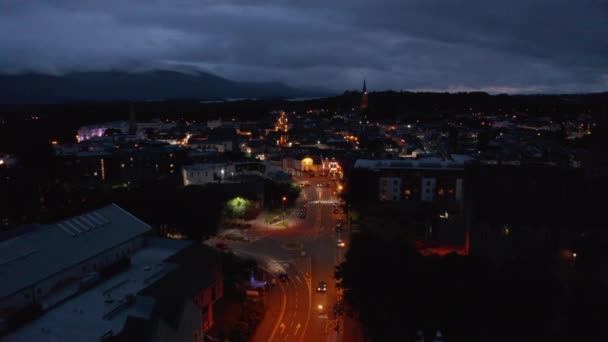 前方の通りオレンジの街路灯によって照らされた上を飛ぶ。夕暮れ時の町の空中ビュー。曇りの空。アイルランドのキラーニー — ストック動画