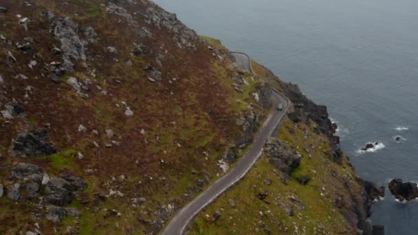 Hoge hoek uitzicht op auto passeren bocht en smalle weg hoog boven de zeekust. Geweldige panoramische route. Ierland — Stockvideo