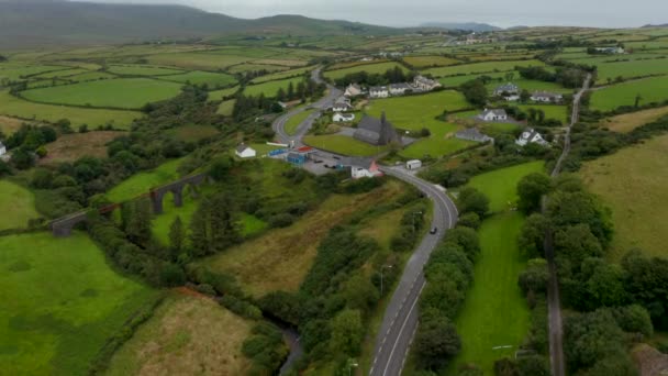 Υψηλή γωνία άποψη της οδικής περιέλιξης μέσα από το χωριό με αραιή ανάπτυξη κατοικιών. Γείρε προς τα πάνω και αποκάλυψε το πανόραμα της υπαίθρου. Ιρλανδία — Αρχείο Βίντεο