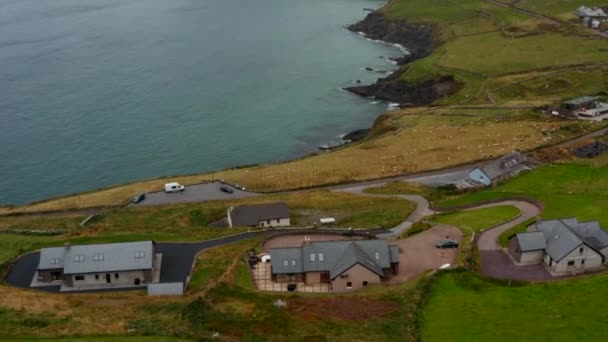 Forwards fly above buildings in countryside near sea coast. Tilt up reveal of peninsula with high cliff. Ireland — Stock Video