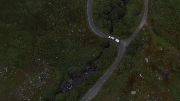 Hoge hoek uitzicht van het voertuig door bochten op smalle weg op het platteland. Vogels oog schot van busje met trailer. Ierland — Stockvideo