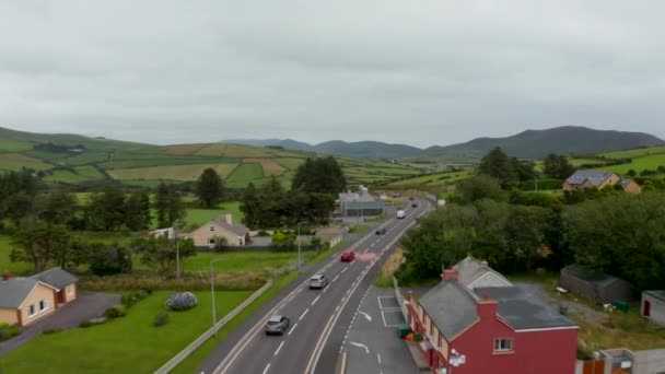 Vpřed sledování skupiny vozidel jedoucích po silnici a projíždějících vesnicí na venkově. Krajinné panorama. Irsko — Stock video