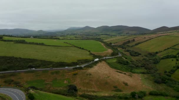 Véhicules conduisant sur la route animée serpentant dans la campagne. Paysage panoramique aérien. Prairies verdoyantes et pâturages. Irlande — Video