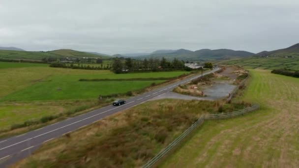 Adiante rastreamento de carro preto dirigindo na estrada em torno de casa grande no campo no dia nublado. Irlanda — Vídeo de Stock
