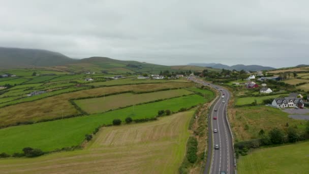 Leť nad rušnou silnicí vinoucí se na venkově mezi pastvinami a projíždějící vesnicí. V krajině je zataženo. Irsko — Stock video