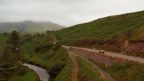 В облачный и туманный день над дорогой пролетает форвард. Автомобили движутся по течению реки в долине. Ирландия — стоковое видео