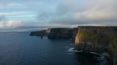 Gün batımında yüksek uçurumların romantik akşam panoramik çekimi. Deniz yüzeyinin üstündeki dikey kaya duvarları. İrlanda 'nın Moher Kayalıkları