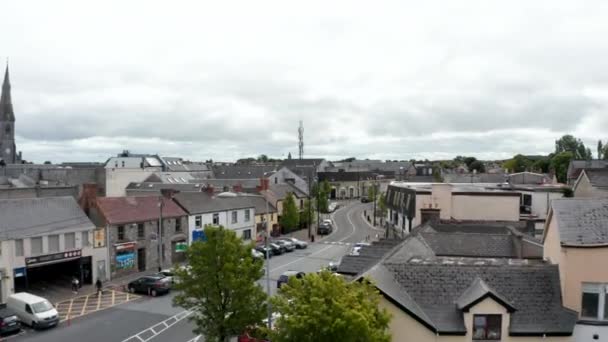 Εμπρός πετούν πάνω από κτίρια και δρόμο στο κέντρο της πόλης. Αυτοκίνητα σταθμευμένα κατά μήκος του δρόμου. Συννεφιασμένος ουρανός. Ennis, Ιρλανδία — Αρχείο Βίντεο