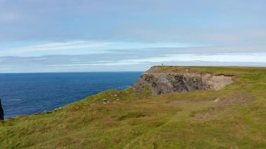 İleriye doğru deniz kıyısının üzerinde uçar. Yüksek kayalıklar dik bir şekilde denize düşüyor. Dalgalar sahile çarpıyor. Kilkee Cliff Walk, İrlanda