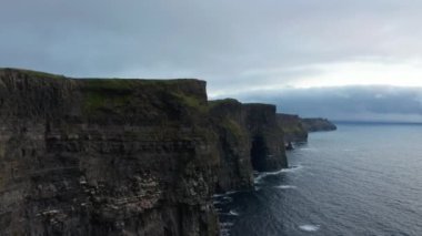 Engebeli kayalık sahil boyunca uç. Alacakaranlıkta dalgalı su yüzeyinin üzerinde yüksek dikey duvarlar. İrlanda 'nın Moher Kayalıkları