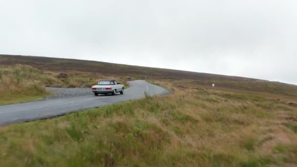 Para a frente viaduto histórico carro esporte dirigindo na estrada curvilínea na paisagem de outono. Prados sob céu nublado. Irlanda — Vídeo de Stock