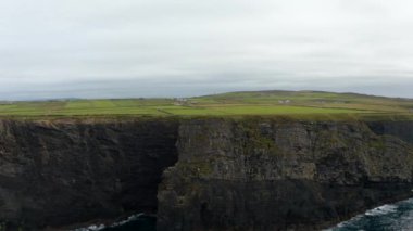 Uçurumun kenarında suyun üzerinde duran turistlerin kayma ve pan görüntüleri. Deniz kıyısında dikey kaya duvarı. Kilkee Cliff Walk, İrlanda
