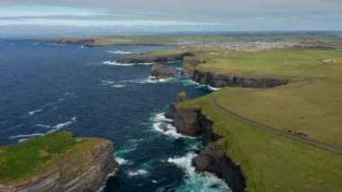 Okyanus kıyısındaki yüksek uçurumların havadan panoramik görüntüsü. Kıyı manzarasının üzerinden geriye doğru uç. Kilkee Cliff Walk, İrlanda