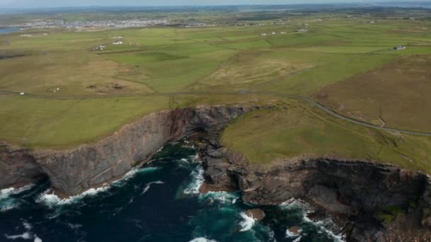 Fotografia panorâmica aérea de prados verdes ao longo da costa marítima. Altos e irregulares penhascos rochosos acima das ondas em queda. Kilkee Cliff Walk, Irlanda — Vídeo de Stock