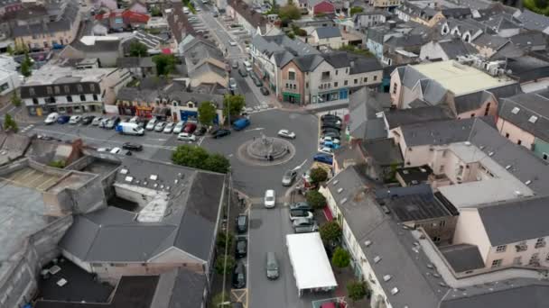 町の中心部のロータリーでのトラフィックの空中上昇映像。広場の周りの建物の前に道路に沿って駐車車。アイルランドのアニス — ストック動画