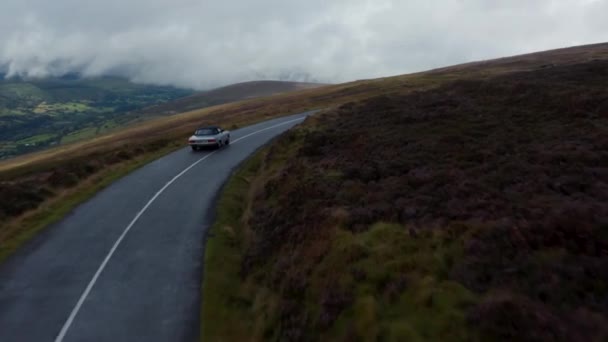 道路の大規模な湿原を巻き。曇りの日にぬれた道路上のヴィンテージスポーツ車の運転の追跡。アイルランド — ストック動画