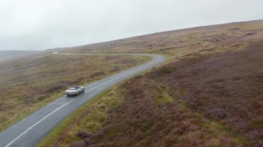 Virajlı yolda otlaklarla çevrili gümüş rengi üstü açılır arabanın izini sürüyorum. Uzak bir yerde kırsal alanda. İrlanda