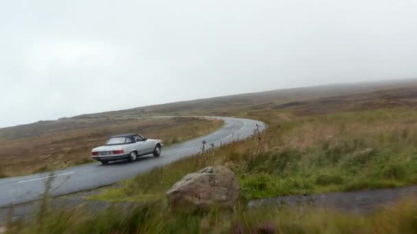 ムーアランズに沿ってぬれた道路上で運転銀ヴィンテージのスポーツカーの前方追跡。秋のかすんで天気。アイルランド — ストック動画