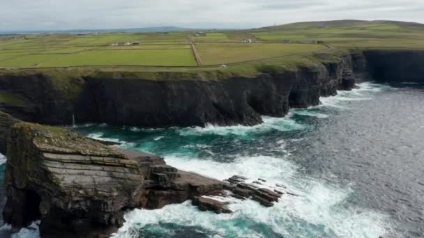 Filmato aerea ascendente della costa del mare con alte scogliere e rotto enormi blocchi di pietra. Inclinare sulle onde lavando rocce. Kilkee Cliff Walk, Irlanda — Video Stock