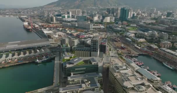 Achterwaarts vliegen boven gebouwen in de haven. Verschillende boten staan op pieren. Tilt up onthullen stadsgezicht en majestueuze Tafelberg. Kaapstad, Zuid-Afrika — Stockvideo