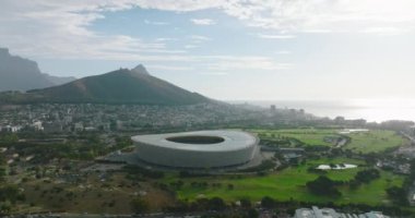 Fütürist yapının kaydırma ve tava görüntüsü. Golf sahasıyla çevrili modern futbol stadyumu. Okyanus kıyısındaki tatil beldesindeki binalar. Cape Town, Güney Afrika