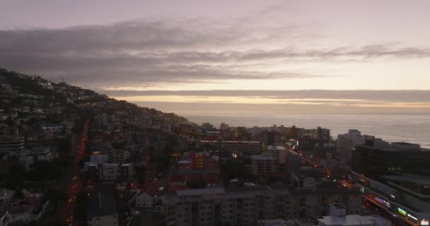 Al crepuscolo volano in avanti sopra il quartiere urbano costiero. Vista aerea contro il colorato cielo al tramonto con nuvole. Città del Capo, Sud Africa — Video Stock