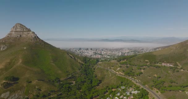 Повітряні падаючі кадри напруженої дороги, що веде до великого міста через гірський перевал. Гора Леви височіє над оточуючим ландшафтом. Кейптаун (ПАР) — стокове відео