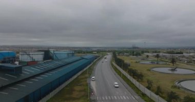 Bulutlu bir günde endüstriyel banliyölerde yol üzerinde uçarlar. Fabrikadaki malzemeler için büyük silindirik tanklar. Port Elisabeth, Güney Afrika