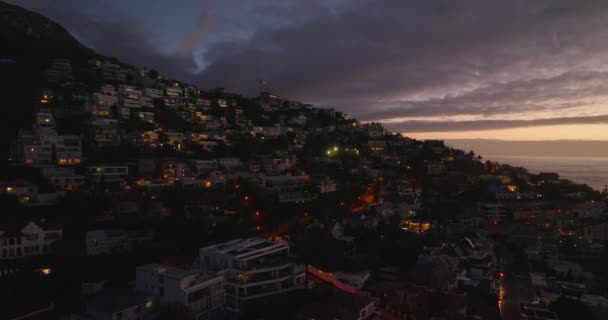 Alacakaranlıkta deniz kenarında lüks mülklerin kaydırağını çek. Pencereler renkli alacakaranlık gökyüzünü yansıtıyor. Cape Town, Güney Afrika — Stok video