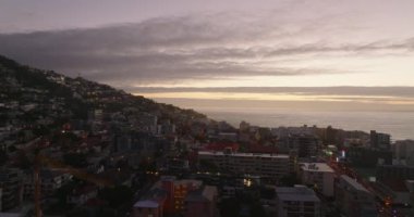 Gün batımında şehrin deniz kıyısındaki binaların kayması. Renkli gökyüzüne karşı çok katlı evlerin havadan görünüşü. Cape Town, Güney Afrika