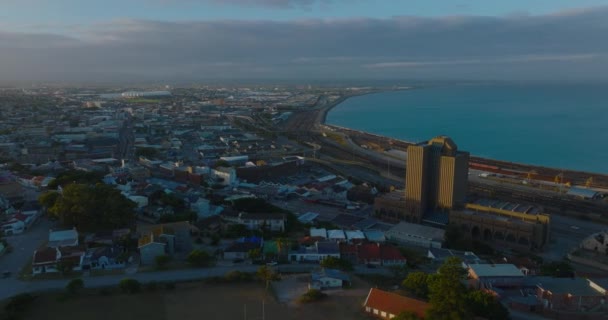 夕日に照らされた高層郵便局ビルの周りを飛ぶ。海の湾での都市の空中映像。ポート・エリザベート,南アフリカ — ストック動画